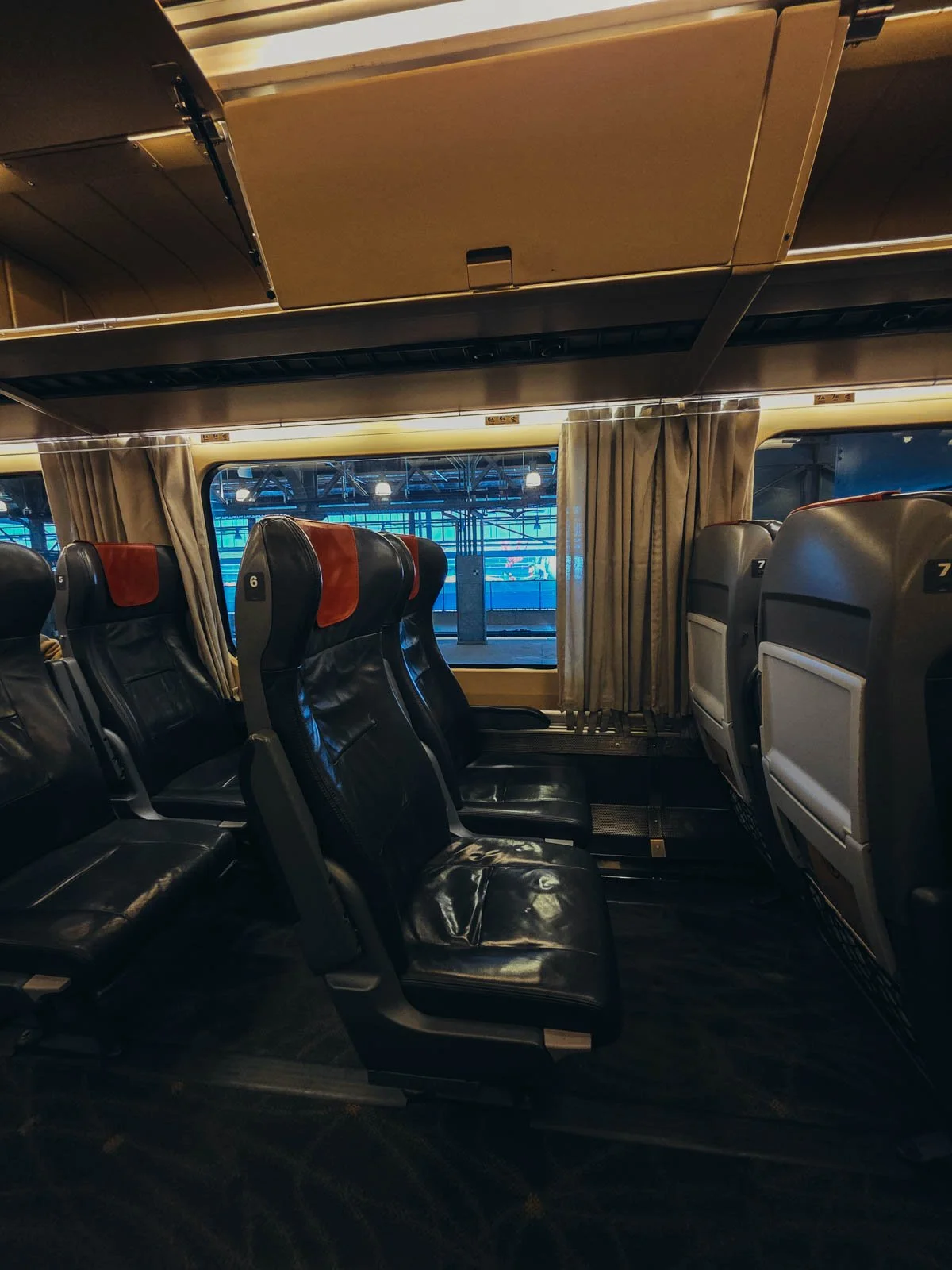 The interior of a economy class train with dark leather chairs and large windows, on a VIA Rail train for our Canada rail trip