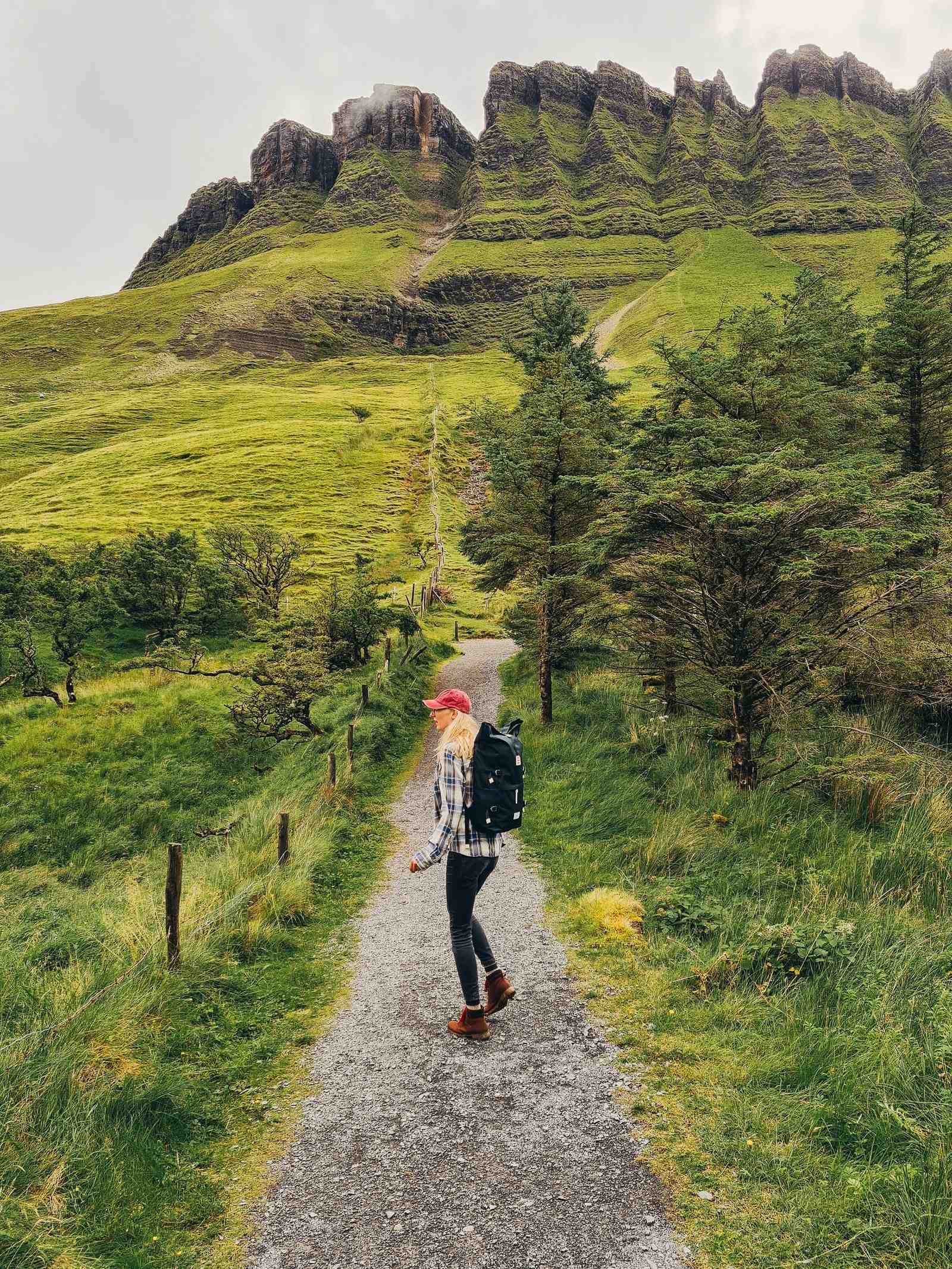 A girl in flannel walking down a gravel pathway with mountains in the background