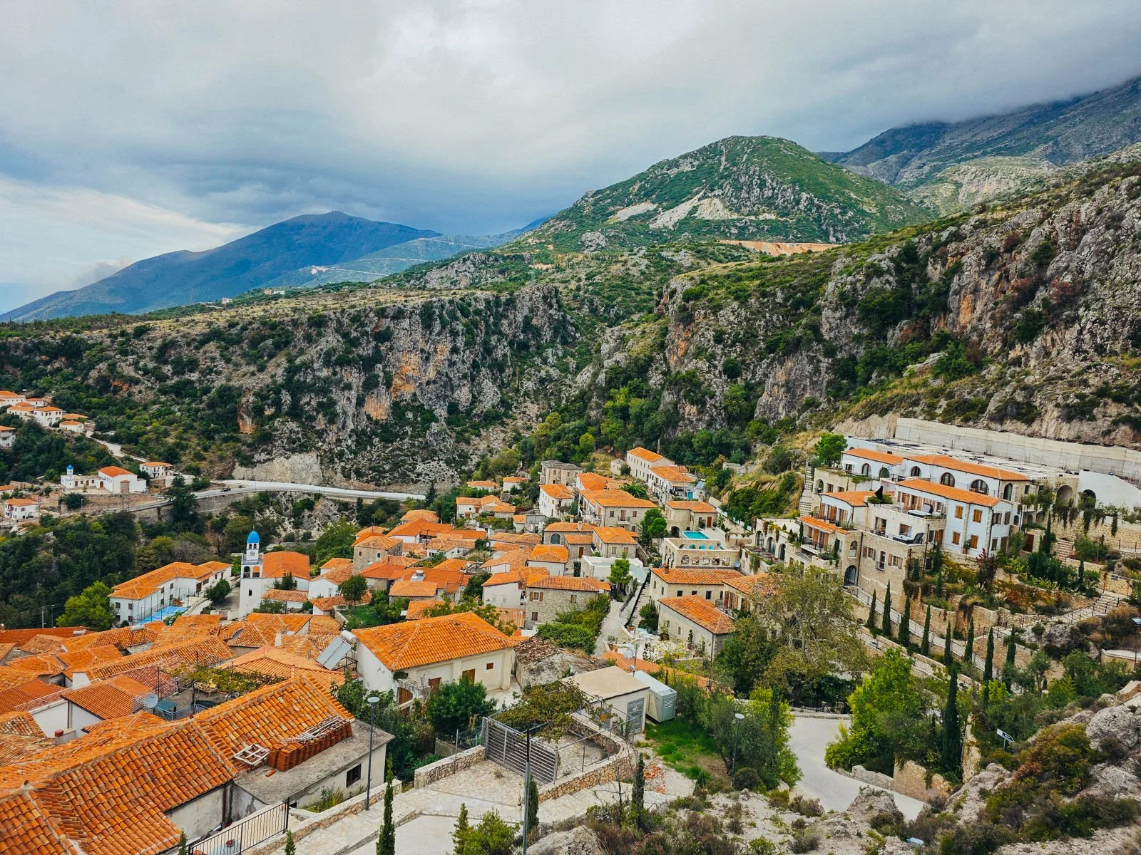 A photo from a hill above a town in South Albania with many buildings of a town with orange tiled roofs surrounded by high rocky cliff walls