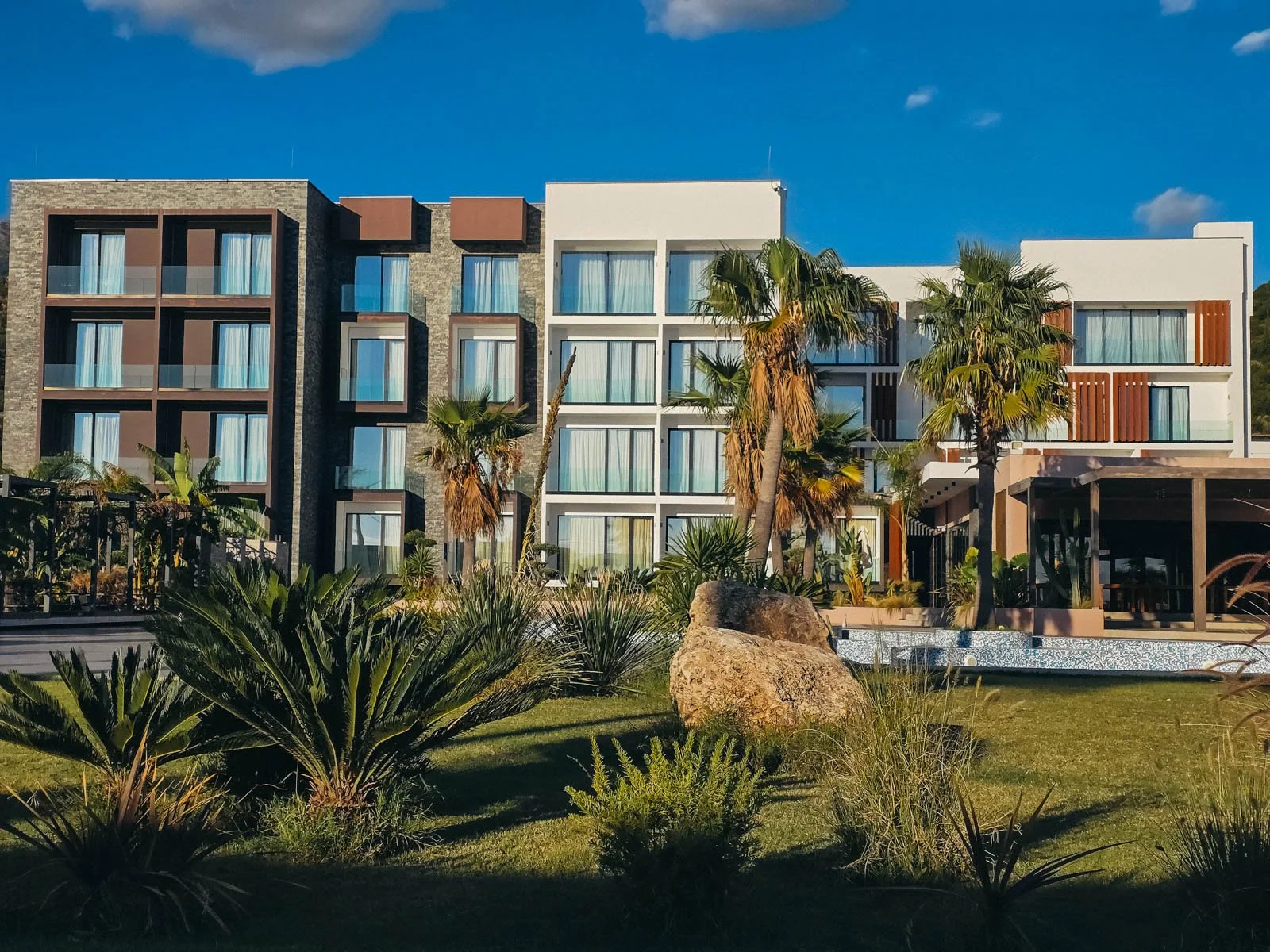 A modern hotel with many windows and a large green lawn with palm trees