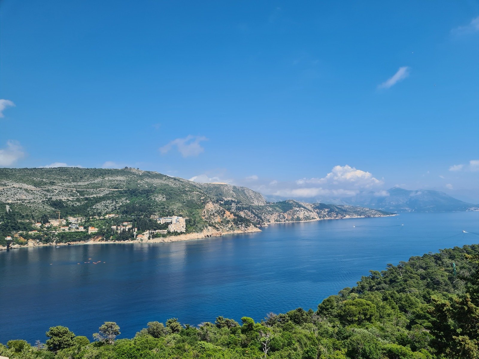 A viewpoint from an island just off the coast of Croatia, looking down the coast of rocky cliffs and greenery next to the blue sea