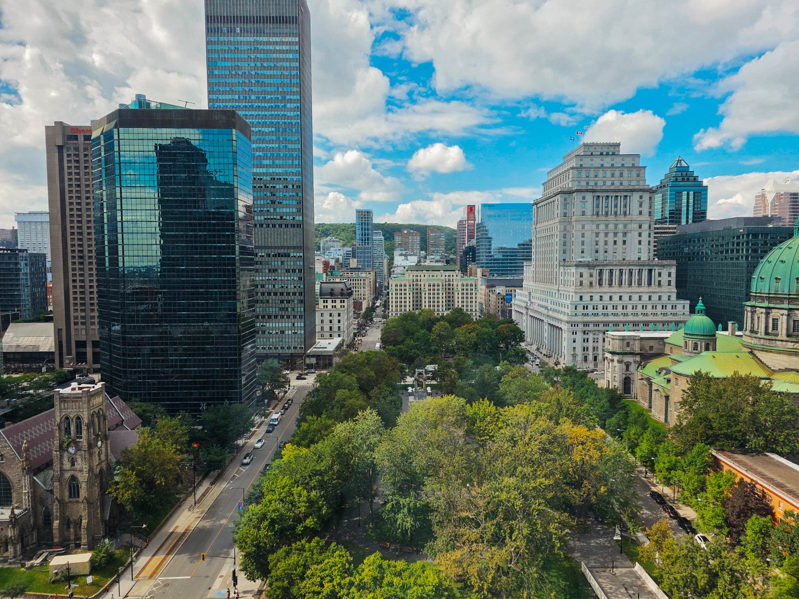An aerial view from our hotel window across downtown Montreal, looking down on a green park area surrounded by tall glass skyscrapers and grand buildings made of stone