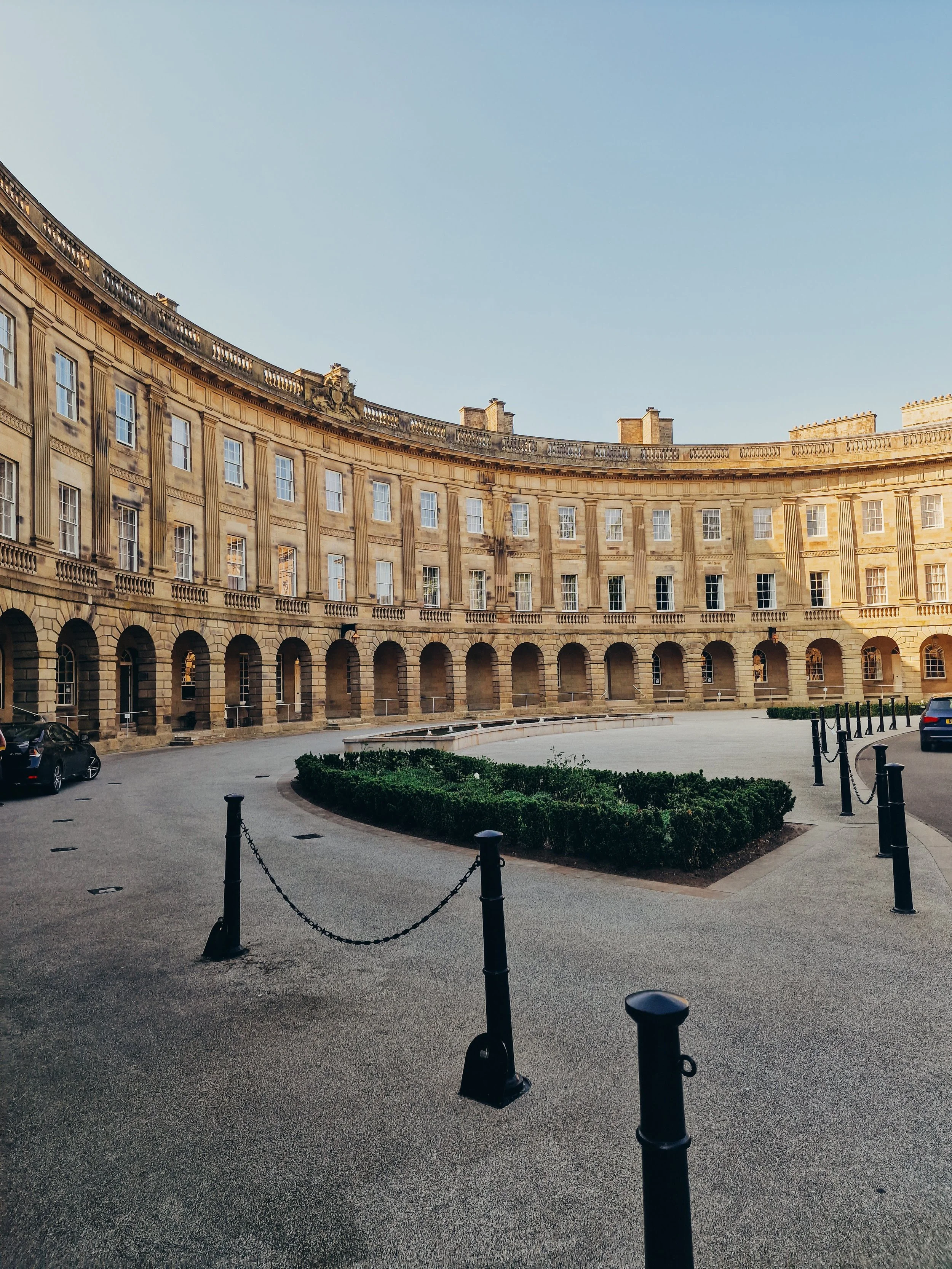 a large, grand sandstone crescent building with a large driveway at the front and one car parked on the left side