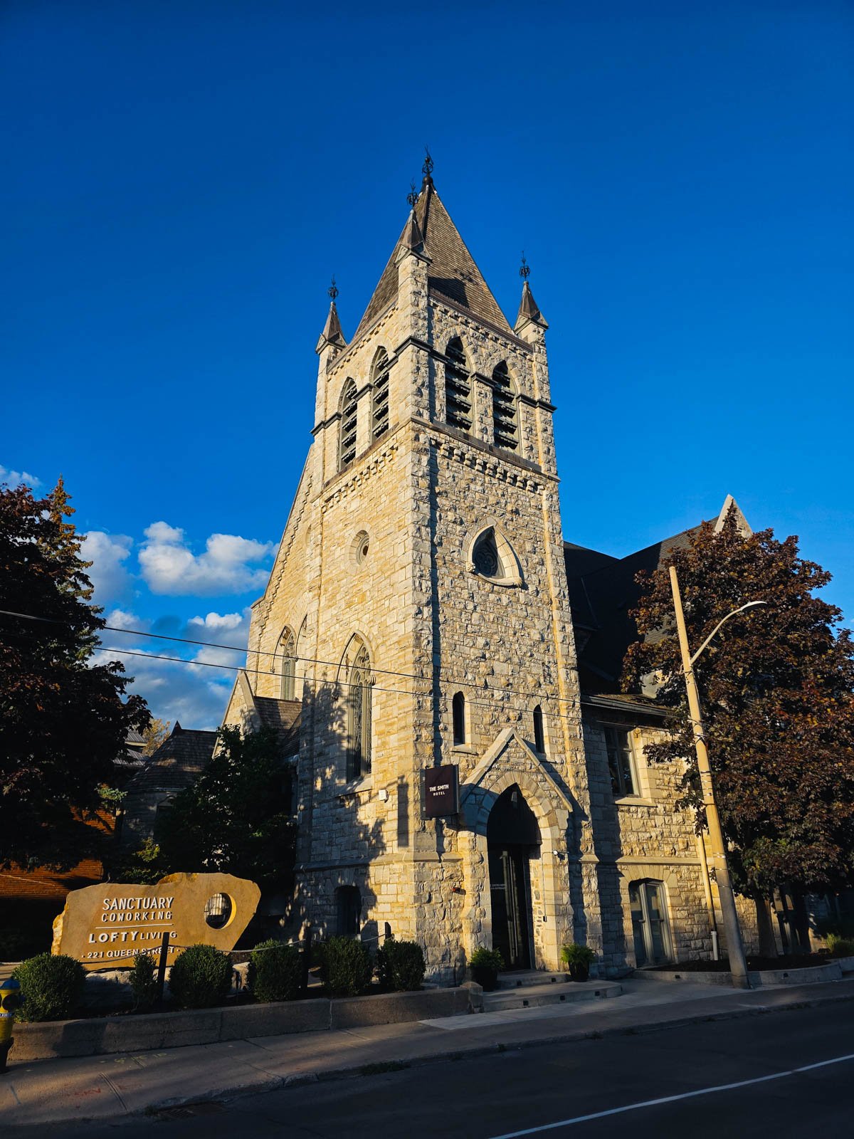 A large stone church that was converted into a hotel on the edge of a street with blue sky behind