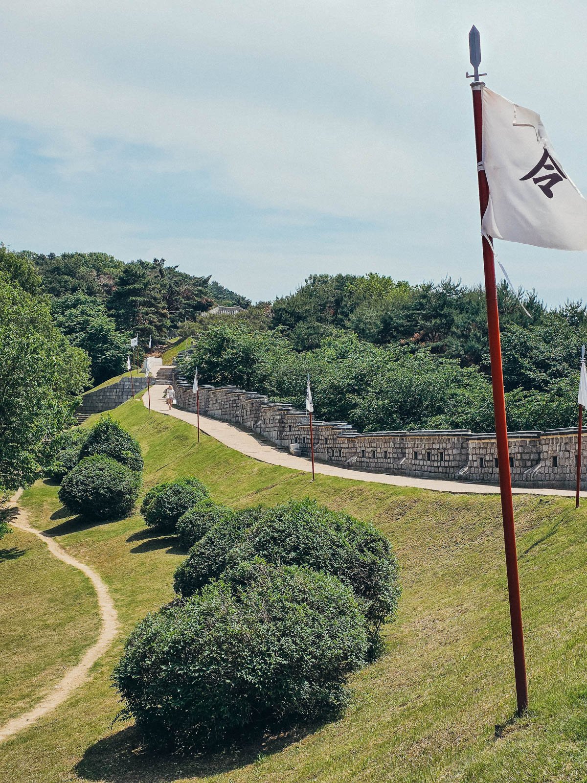 A fortress wall running along a green hill with many trees in the distance