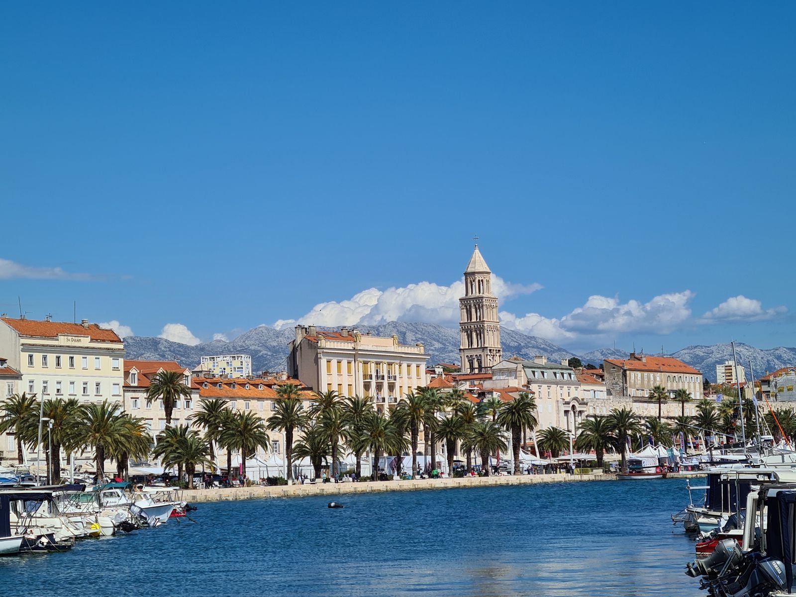 skyline of Split Croatia old town with orange rooftops and the bell tower dominating. Sky is blue and the view is looking across water where boats are docked