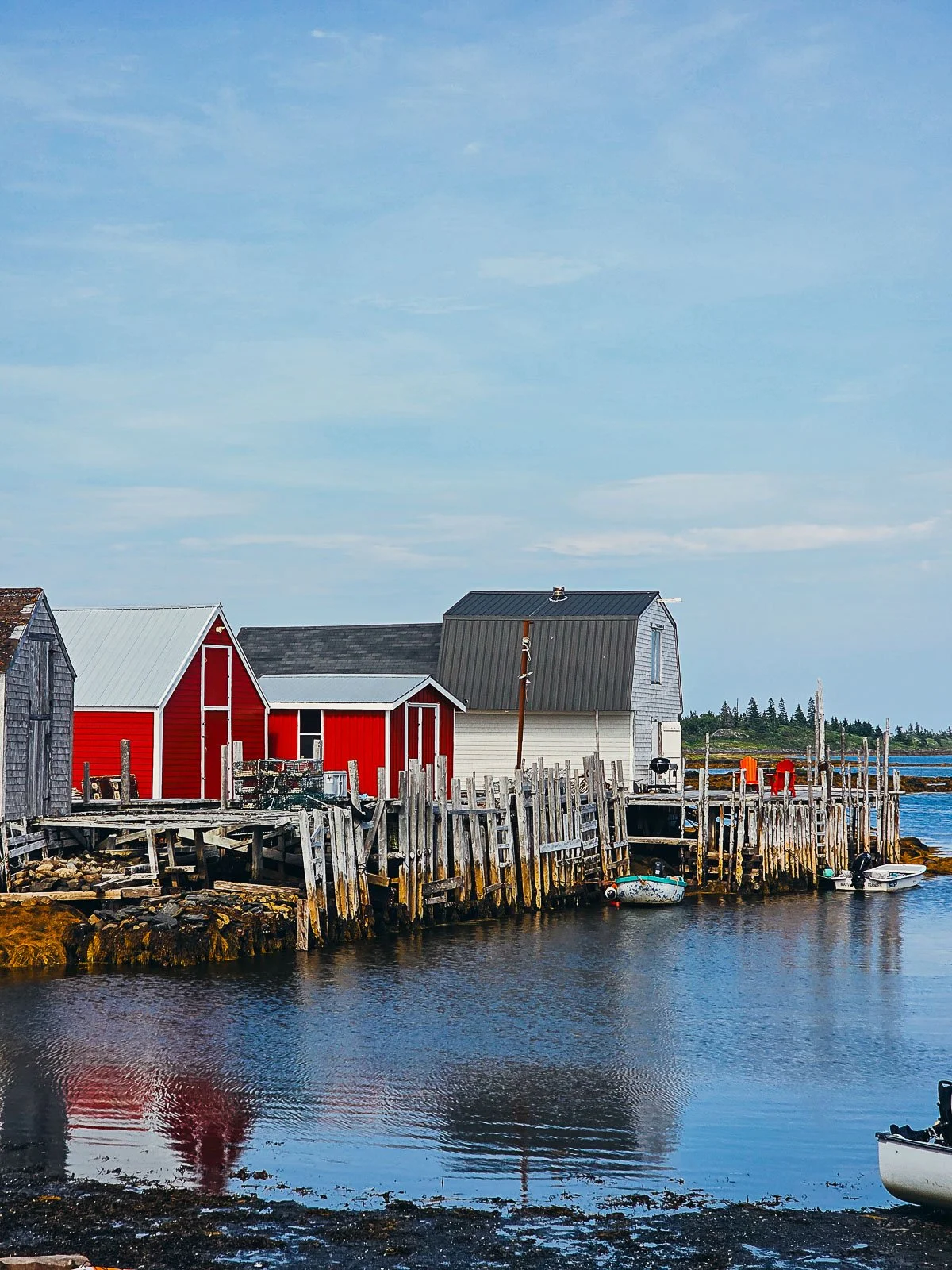 red and white boat houses on wooden stilts along a harbour with the tide partially out