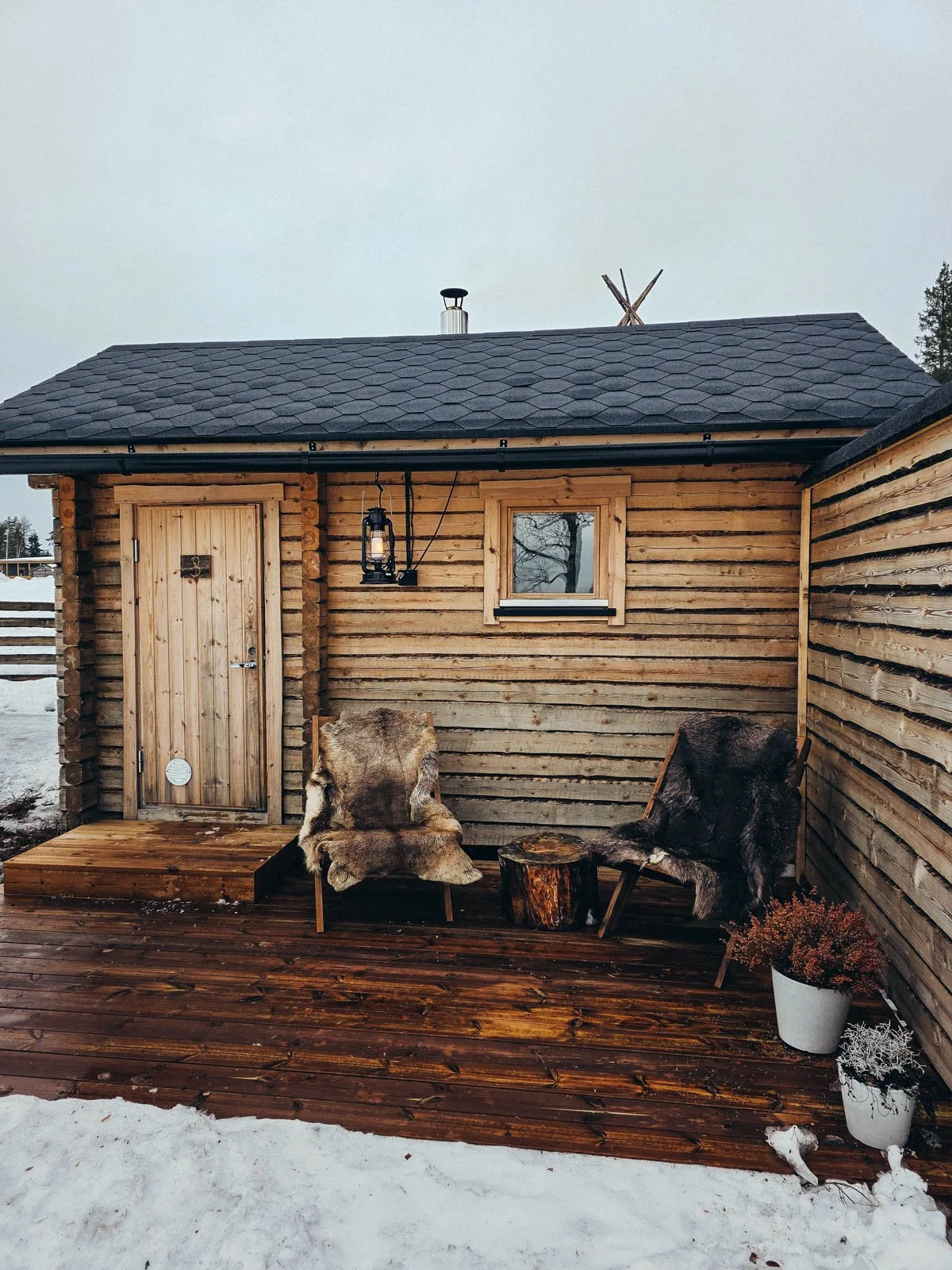 A small wooden private sauna building with a deck and fur covered chairs surrounded by snow - a must do experience on a Finland winter itinerary