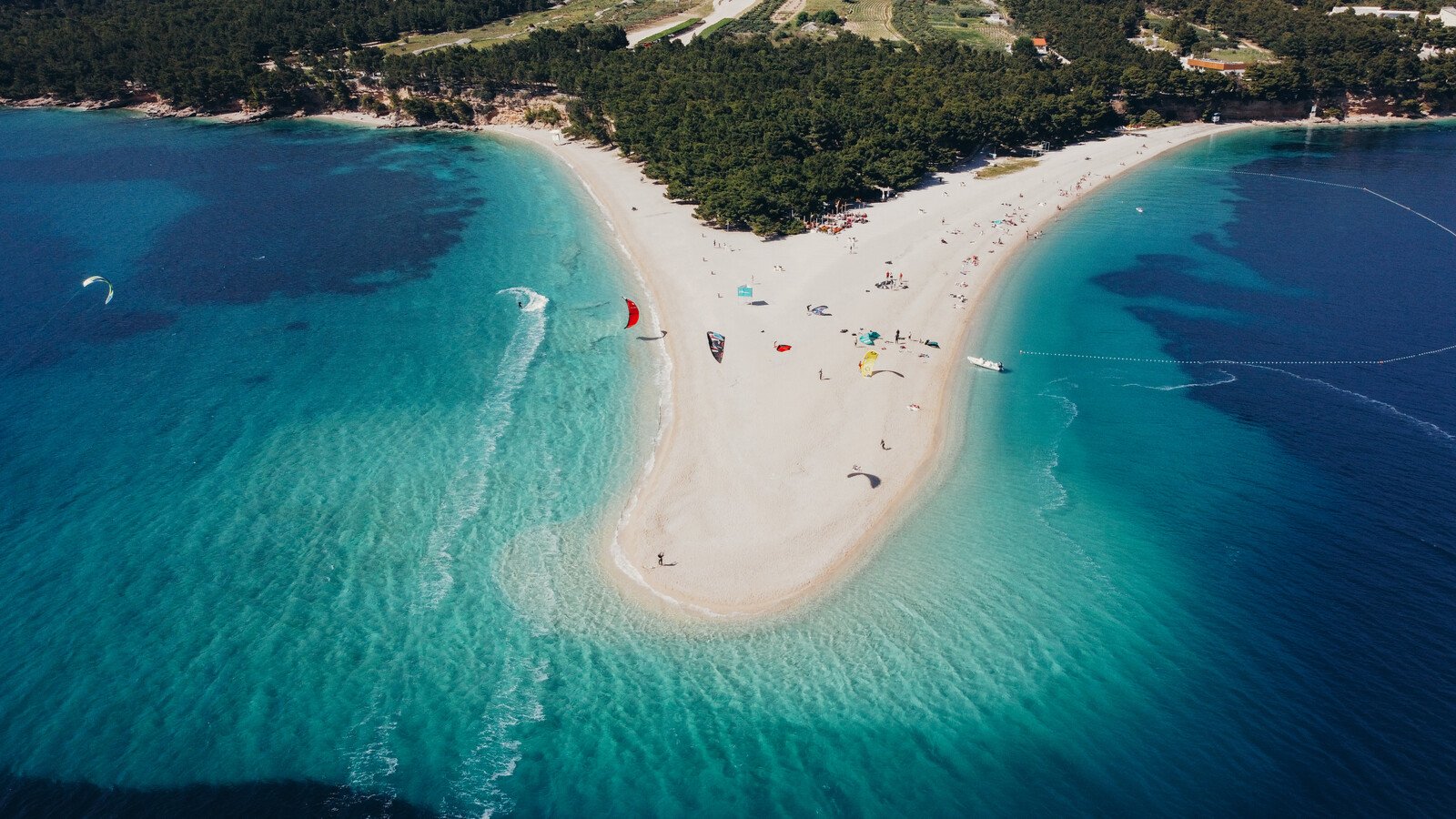 a sand bar beach jutting out from the coast into turquoise blue water with wind surfers visible