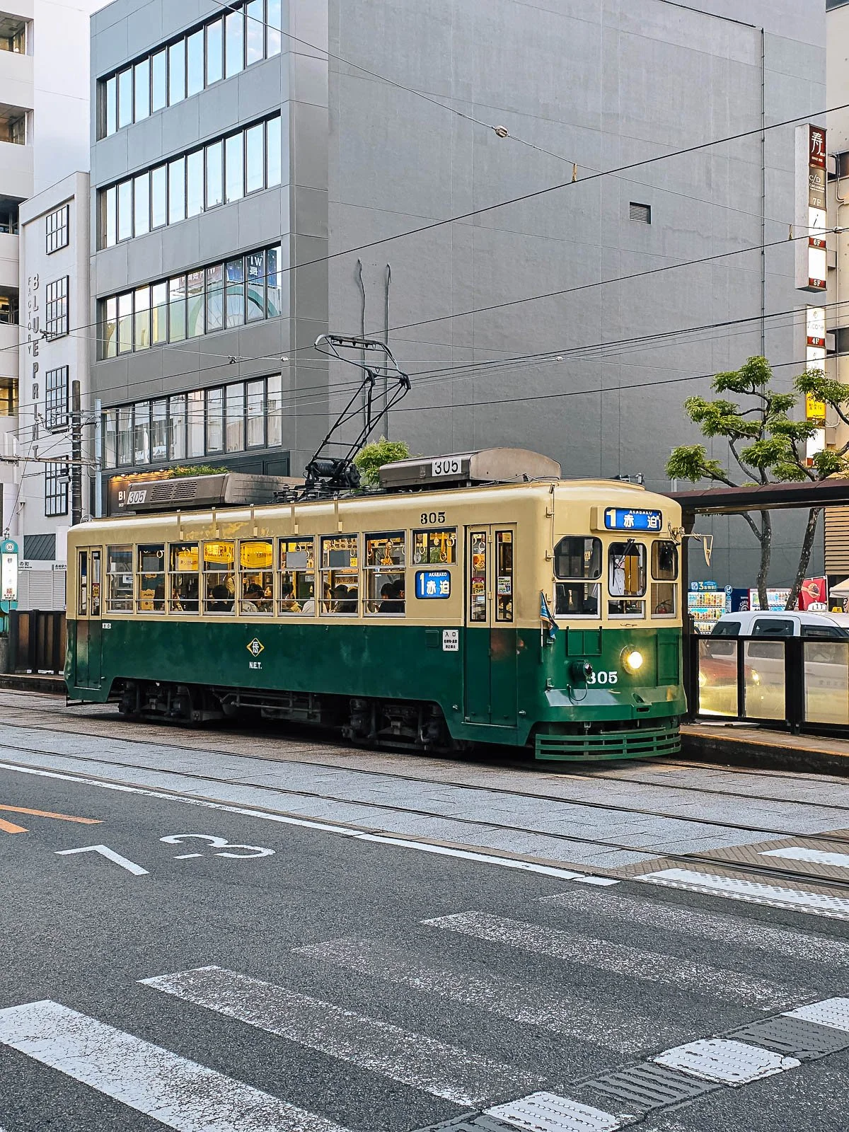 An old yellow and green tram in Nagasaki, stopped at a tram stop to pick up passengers on the street