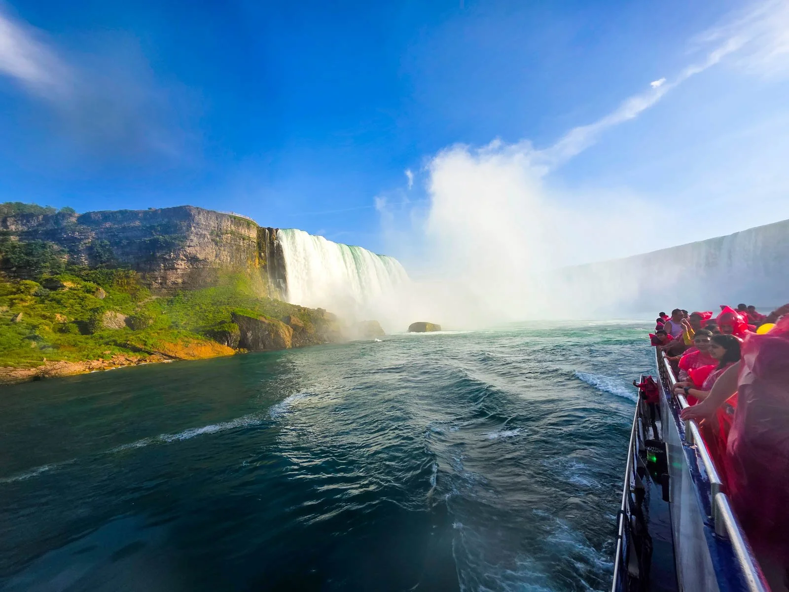 People on a boat in red ponchos with blue water and the large Niagara Falls in the background