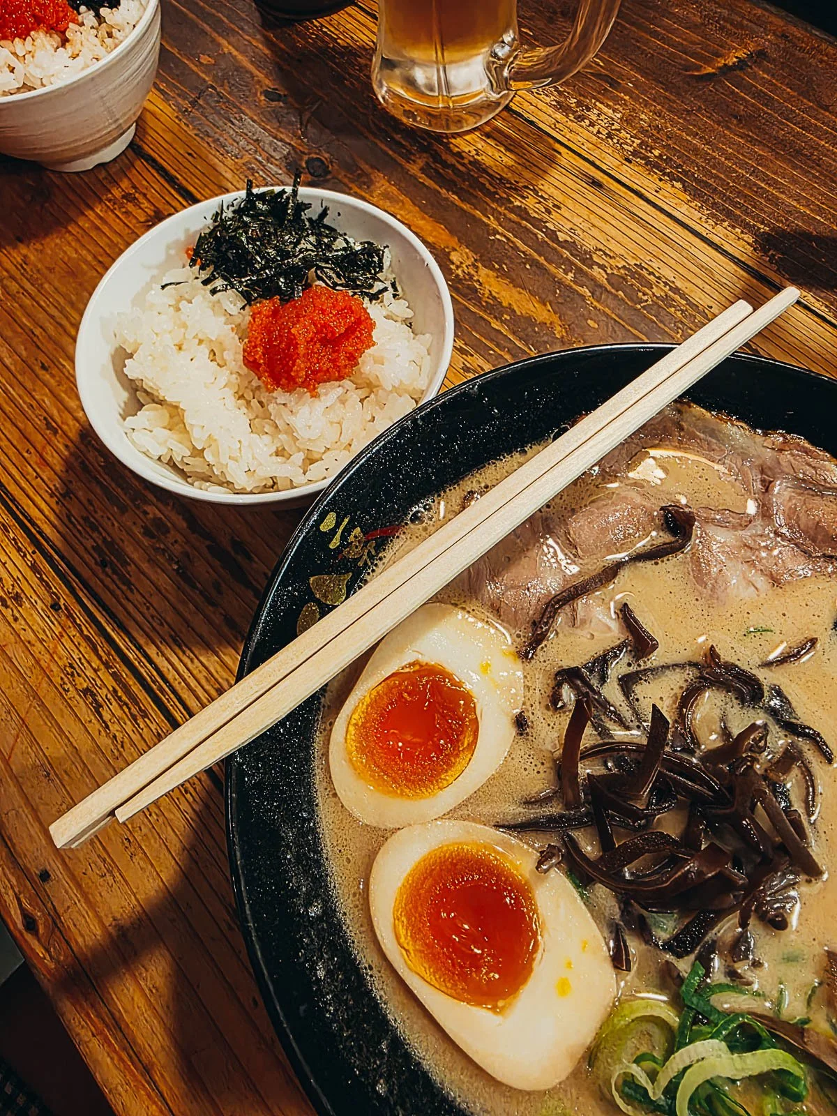 A bowl of ramen with a brown cream broth with eggs and chop sticks on a wooden table
