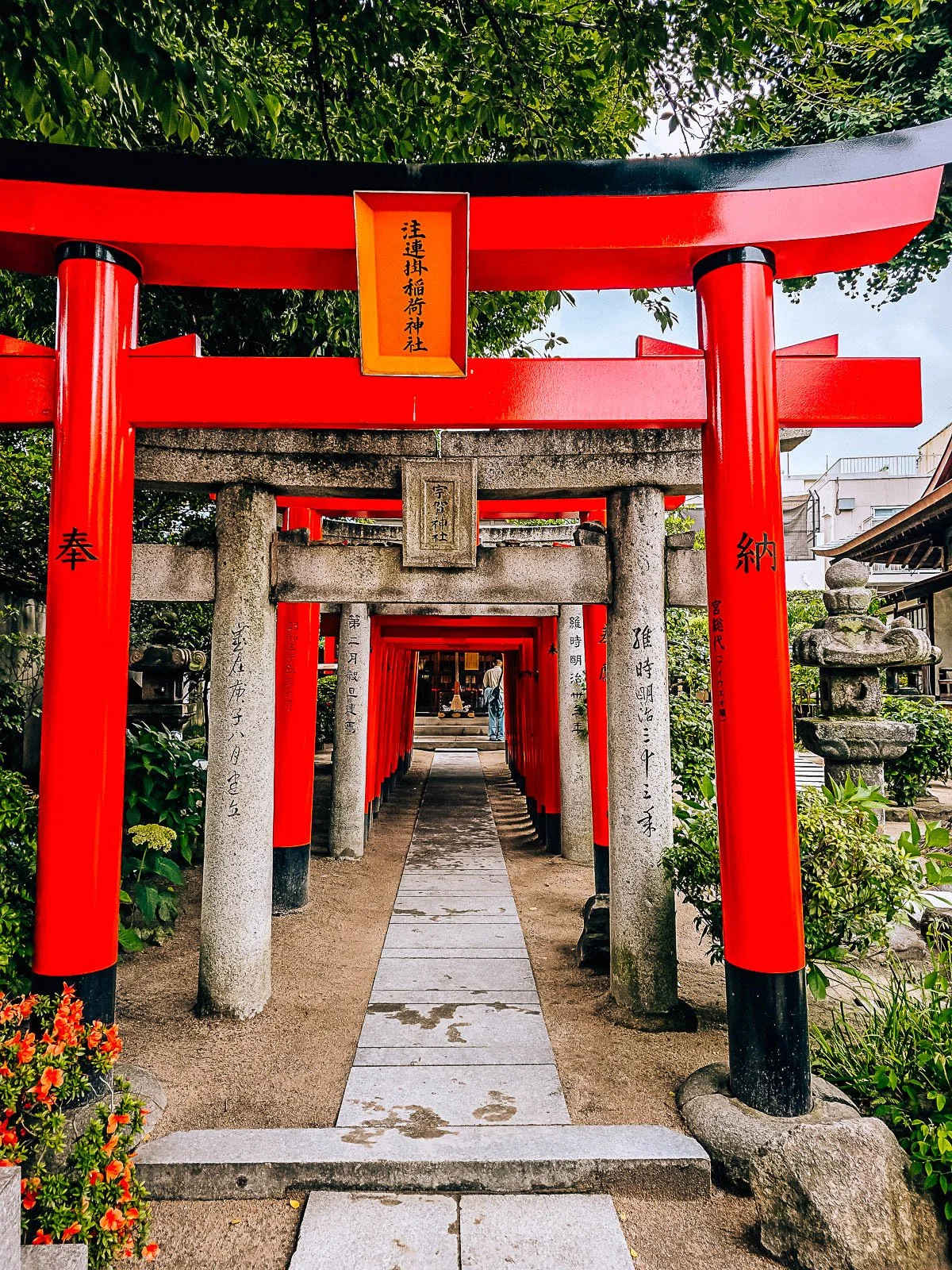 Alternating orange and stone torii gates covering a small pathway lined by gravel at Kushida temple in Fukuoka