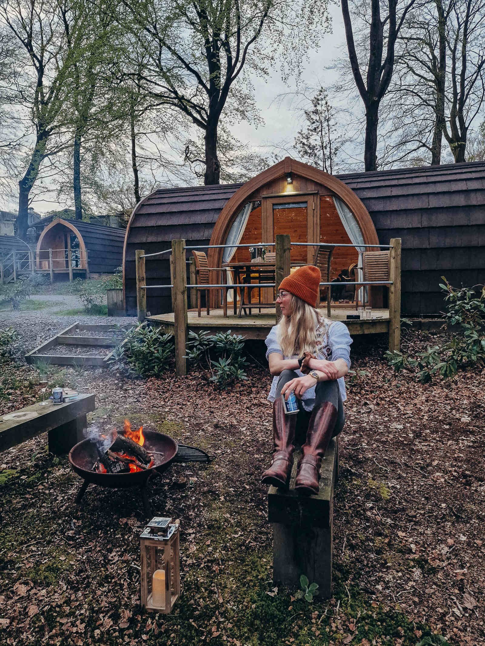 a smoking fire pit with a wooden glamping lodge surrounded by woodland in the forest of bowland