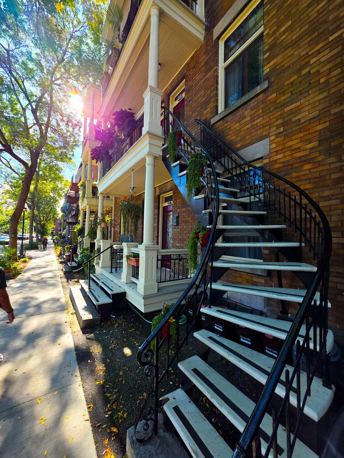A curving staircase leading to the top floor of a house porch on beautiful Victorian style houses on a quiet residential street with trees