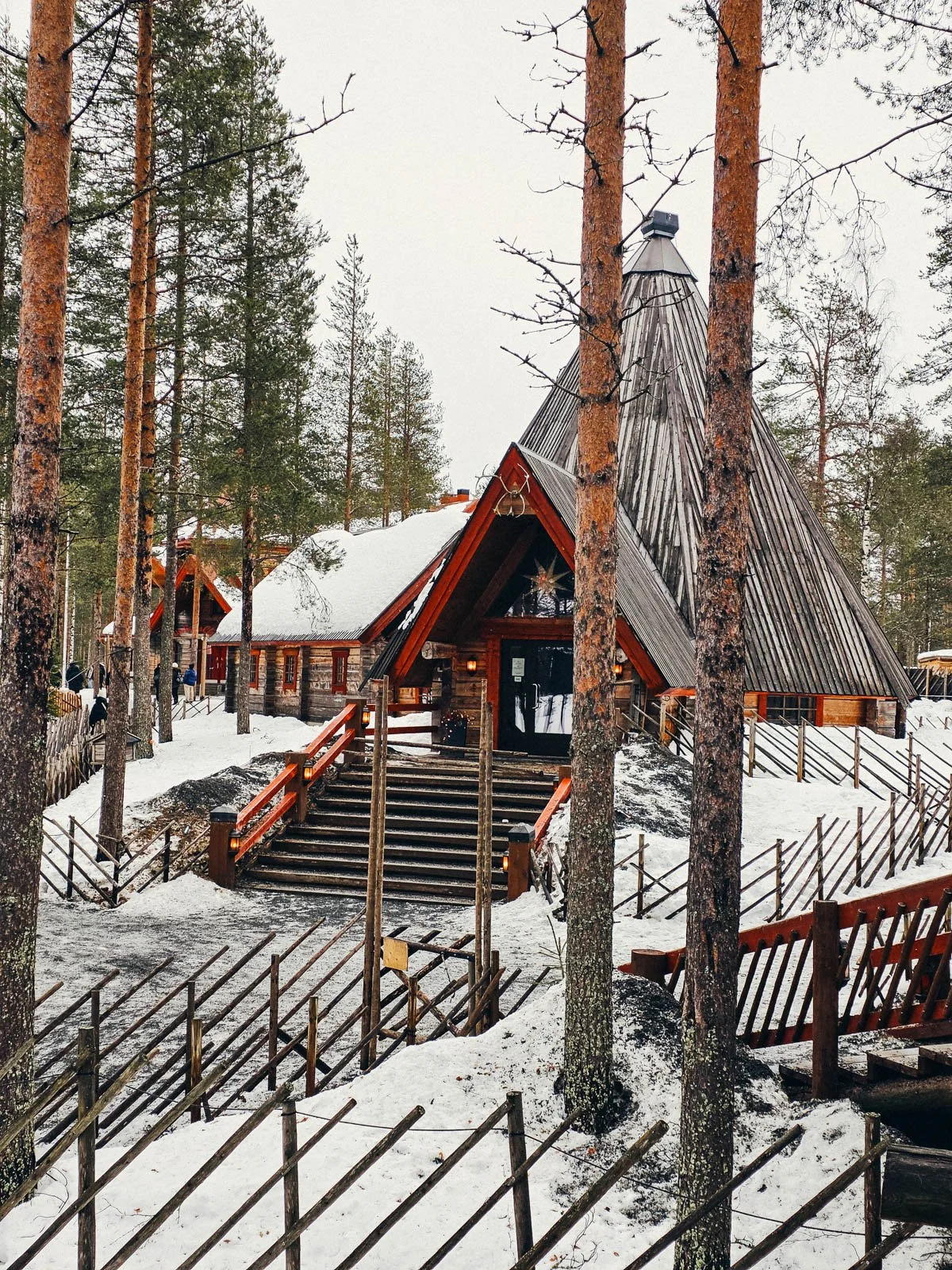 A large wooden building with a steep pointed wood roof surrounded by snow and pine trees
