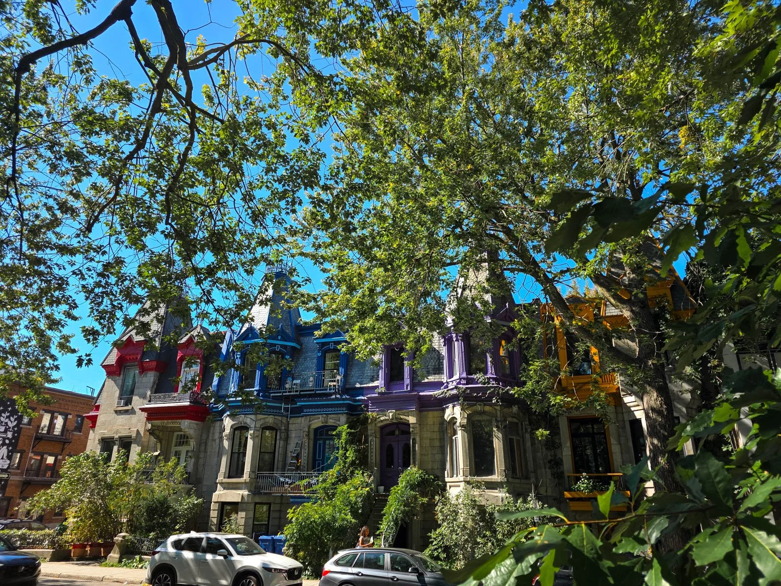 Big houses in Montreal with colourful roof turrets in red, blue, purple and orange, on a leafy street in Montreal