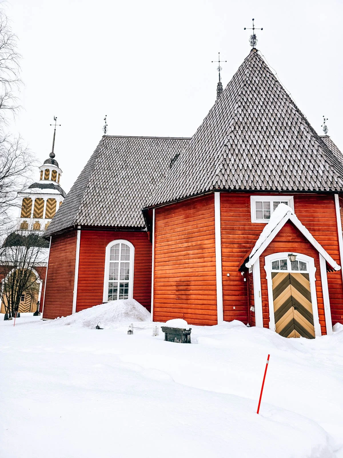 A large red wooden church with a steep roof surrounded by snow