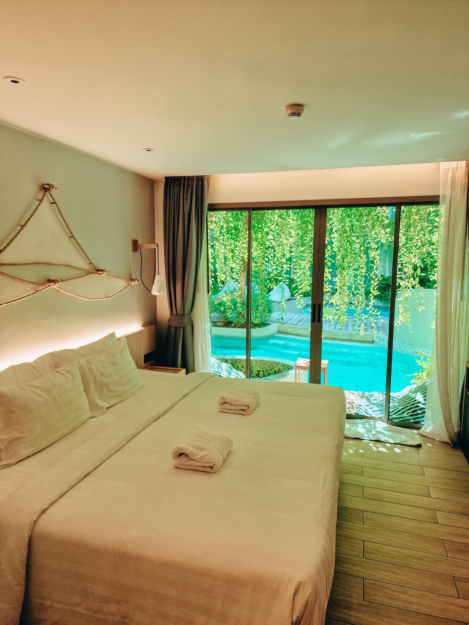 a hotel room bed with a view of the pool outside the glass door