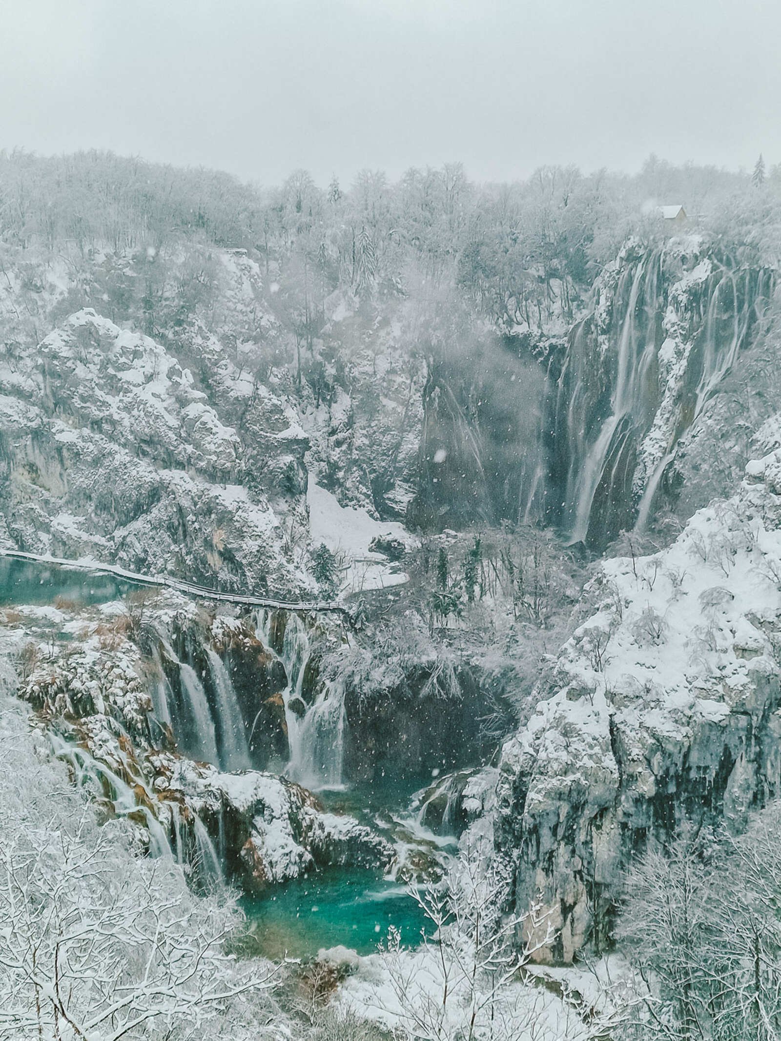 View from a viewing platform of Veliki Slap waterfalls falling in multiple places down a steep cliff into a turquoise blue lake below