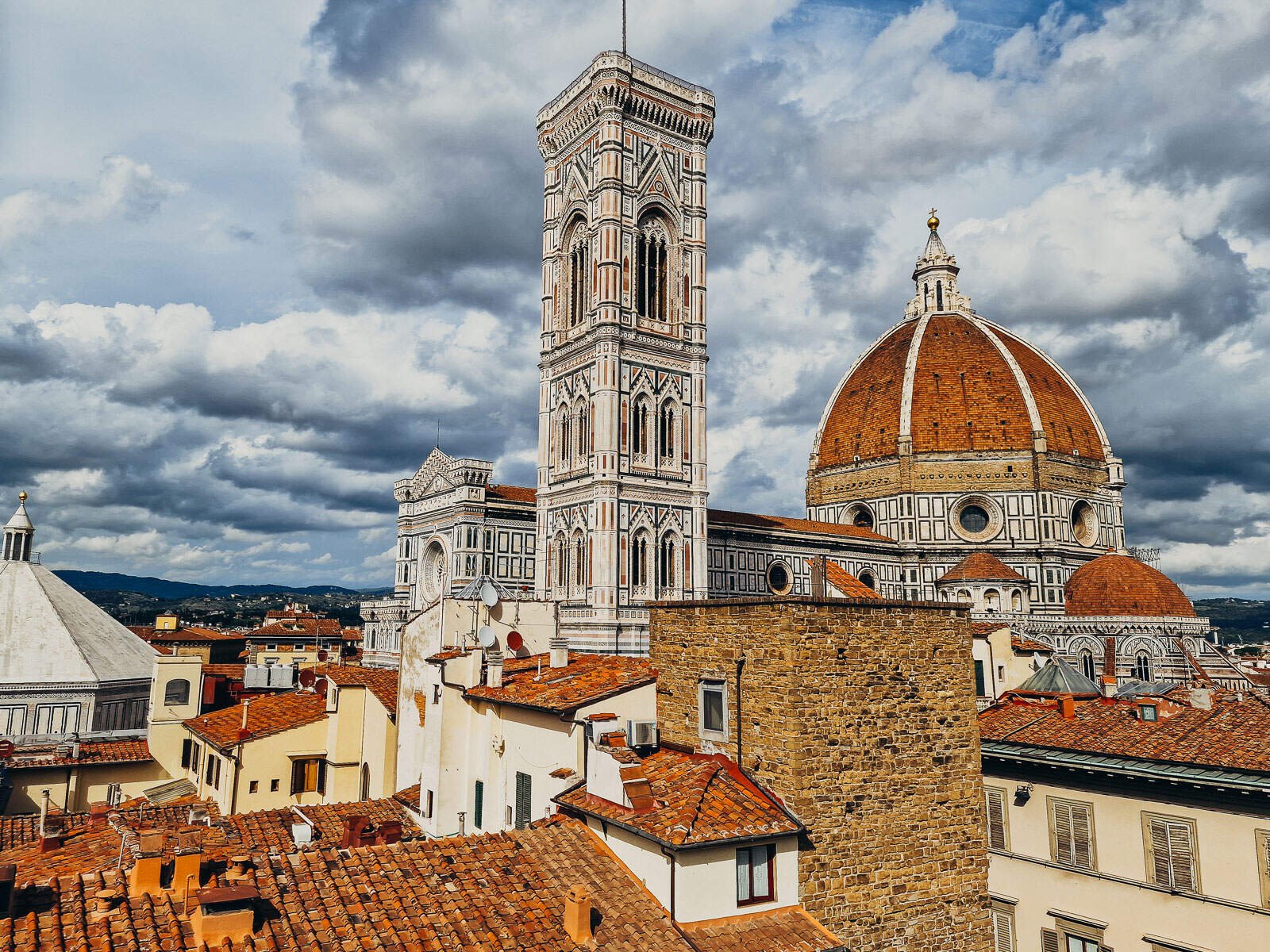 A view across roof tops of the famous dome and tower of the Florence Duomo in Italy with terracotta orange dome and black detail architecture