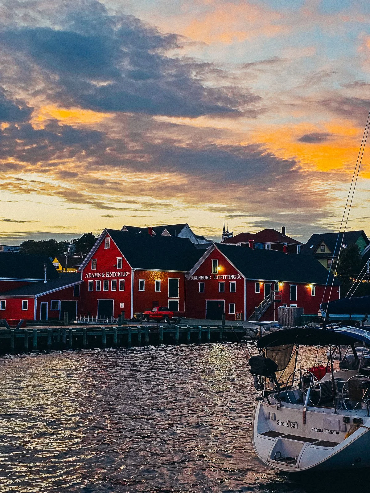 Red fishing wharf buildings with the sun setting behind and the water in the foreground
