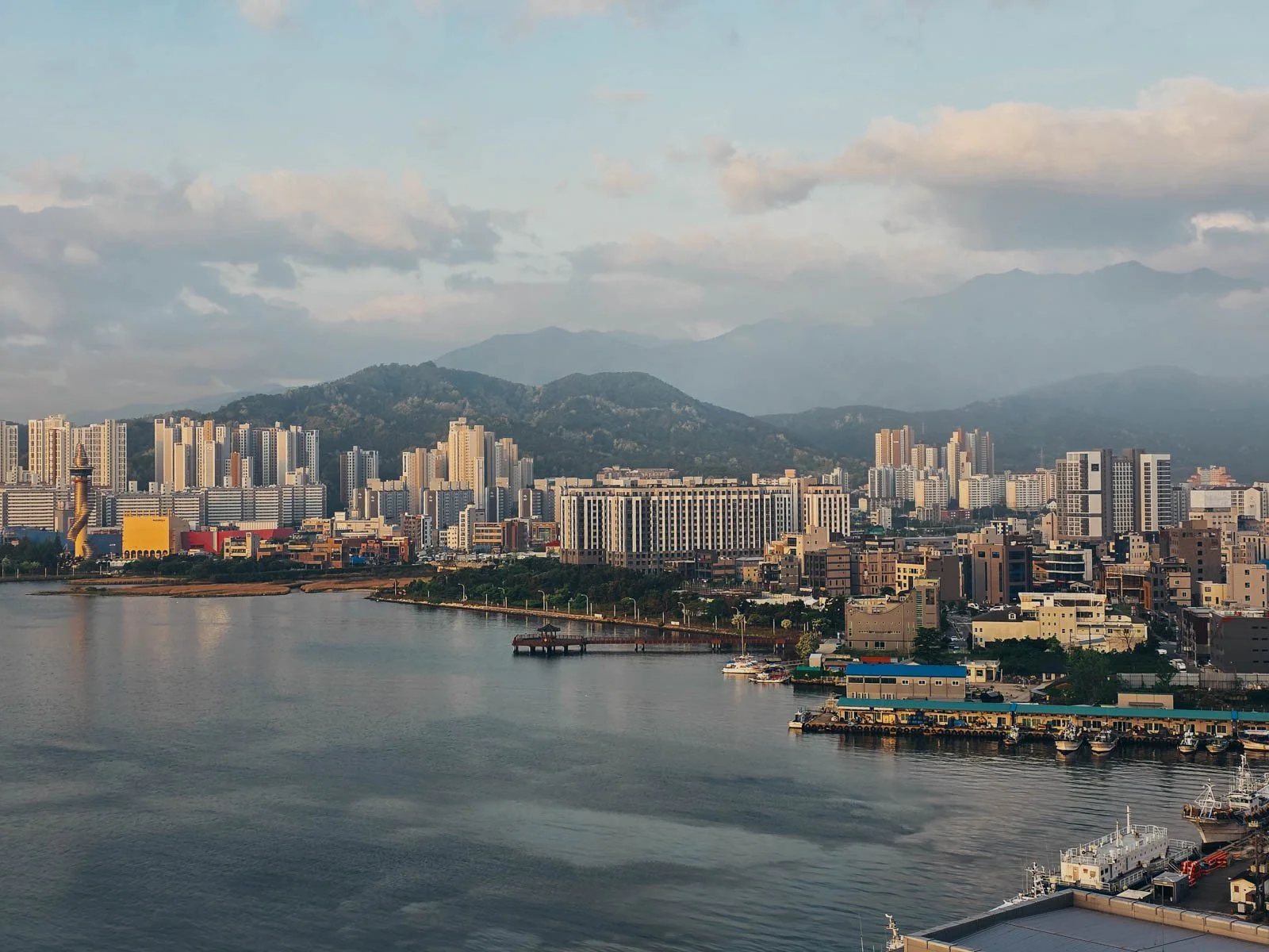 A city skyline at the edge of a lake at sunrise. In the background a tree covered mountains with low cloud and mist partially obscuring them