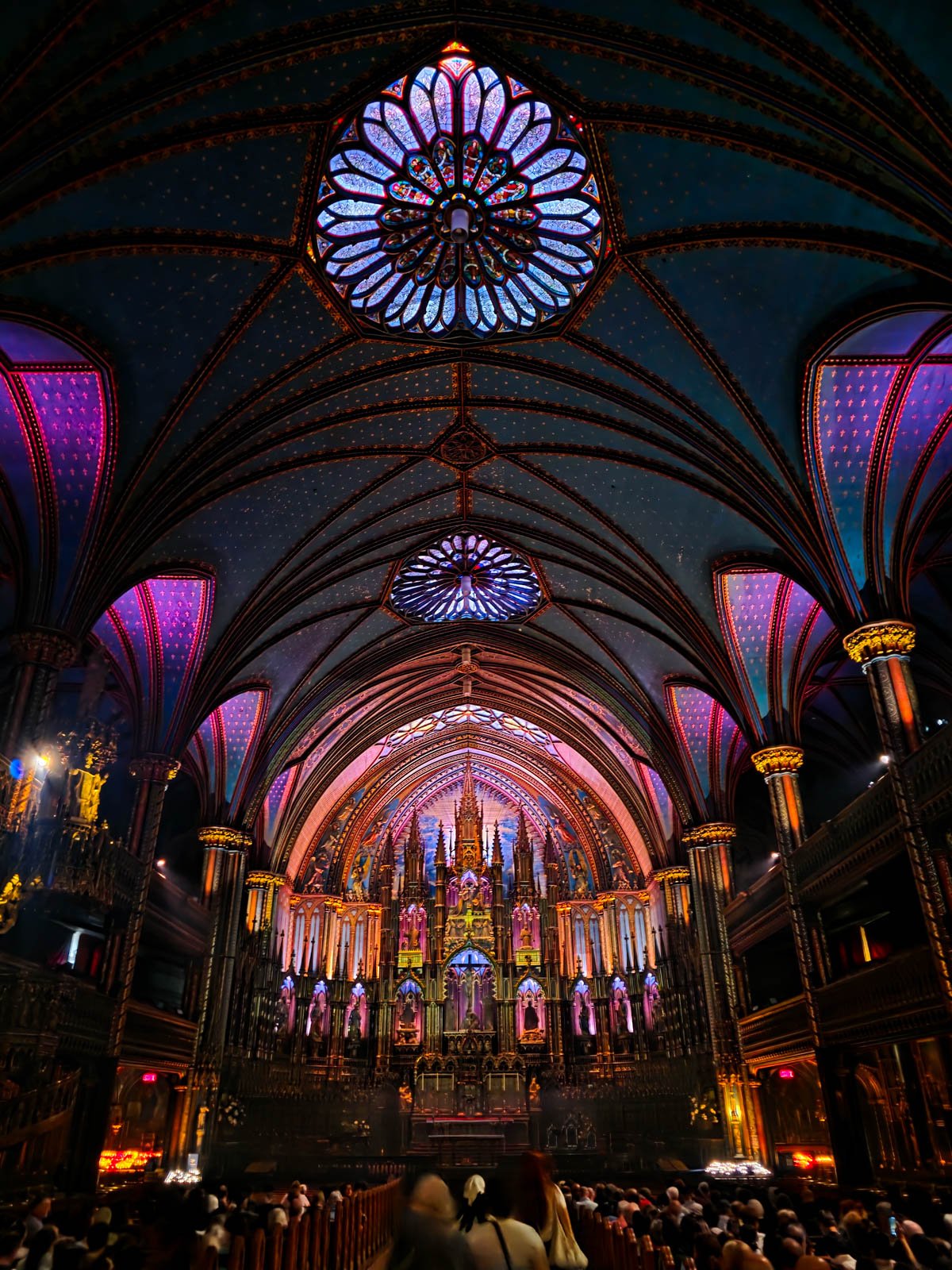 Inside a darkly lit cathedral with lighting on the ceiling arches and religious decor that make it look like it's glowing in pink, blue and purple