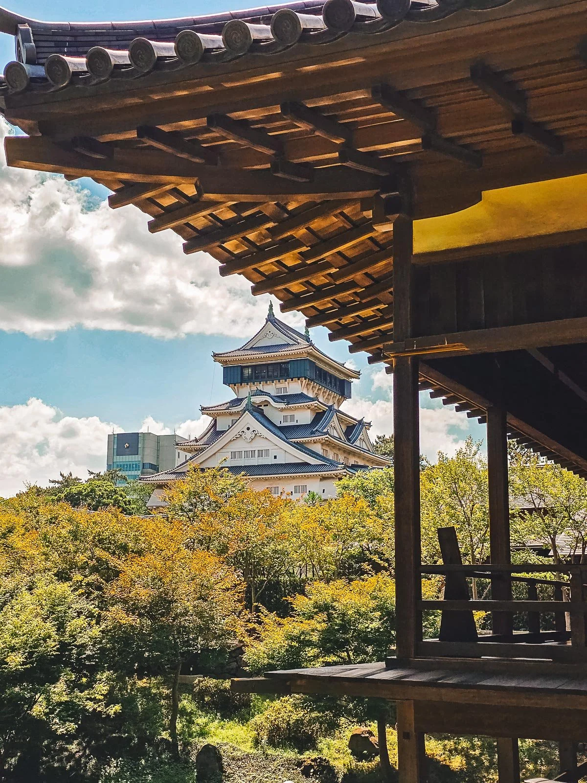 a traditional Japanese castle seen from a Japanese garden with a traditional wooden structure visible in the foreground