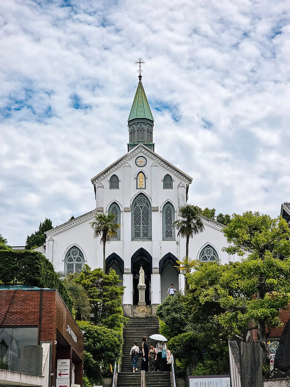 A large white church with a green spire at the top of a set of steps - Oura Catholic Church in Nagasaki