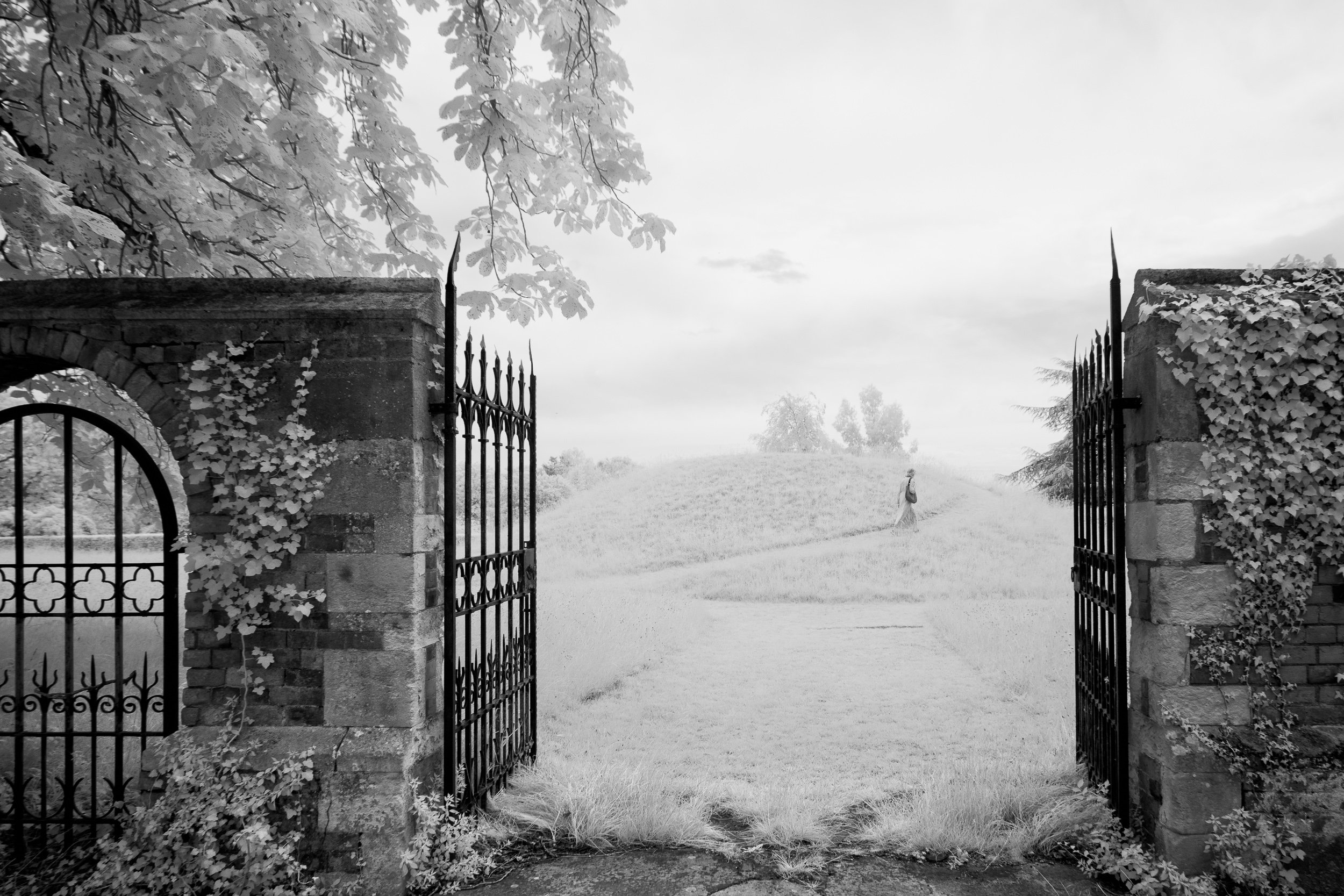 Spooky infrared image of a lady walking in the distance through an ancient gate at an English country home