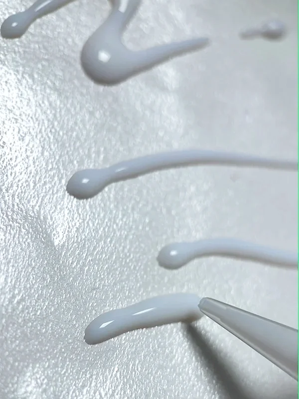 Adhesive applied in the desired eyeliner shape on a transparent plastic sheet as part of creating metallic eyeliner swatches for face charts.