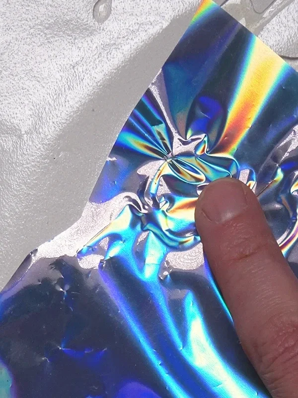 Pressing holographic foil gently onto dried adhesive eyeliner shapes to create metallic effects for face charts.