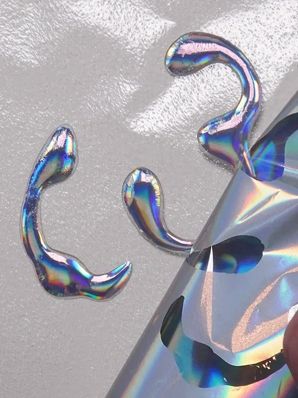 Lifting holographic foil to reveal metallic eyeliner shapes, repeating application where needed for face chart designs.
