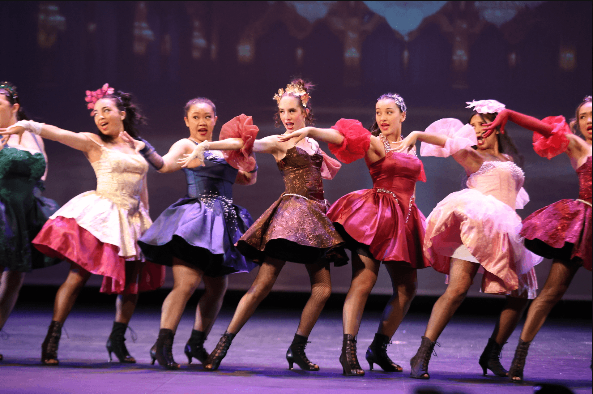 Group of women ballet dancers on stage wearing colorful costumes with full skirts, performing a choreographed dance in unison.