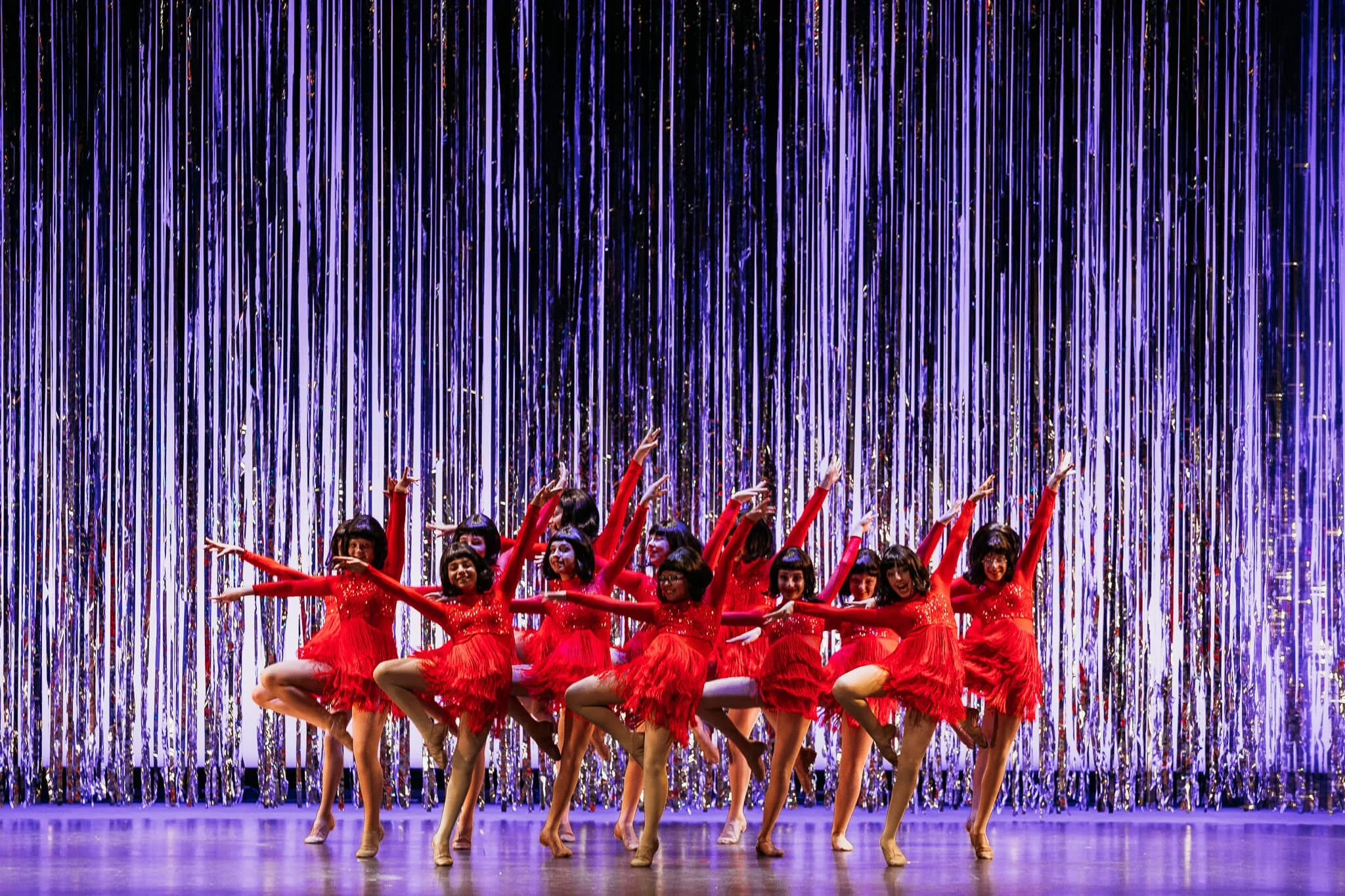 Group of children in red costumes performing a dance in front of shiny purple streamers.