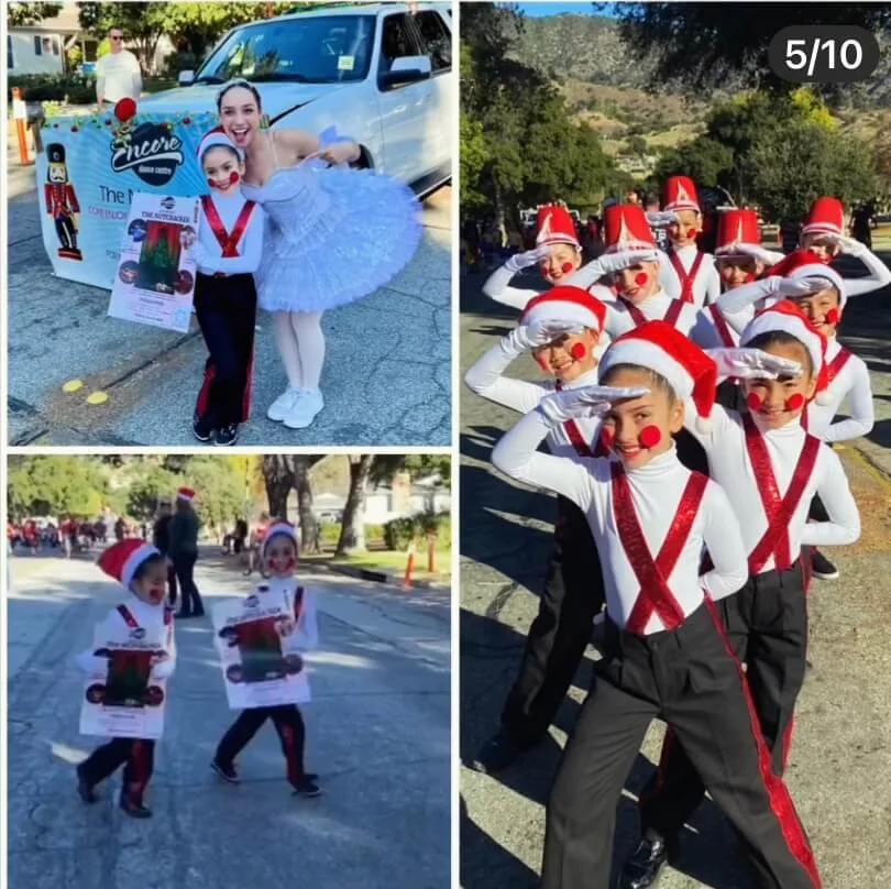 A group of young children dressed as toy soldiers with red hats, red pom-pom noses, and white and red uniforms, participating in a parade outdoors, with trees and people in the background.
