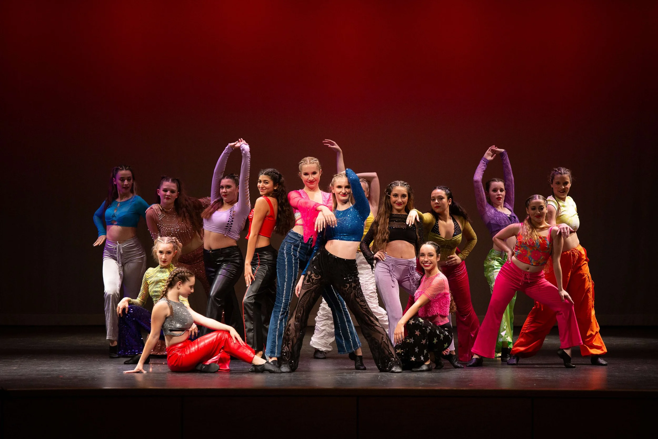 Group of dancers on stage in colorful costumes, posing for a photo after a performance.