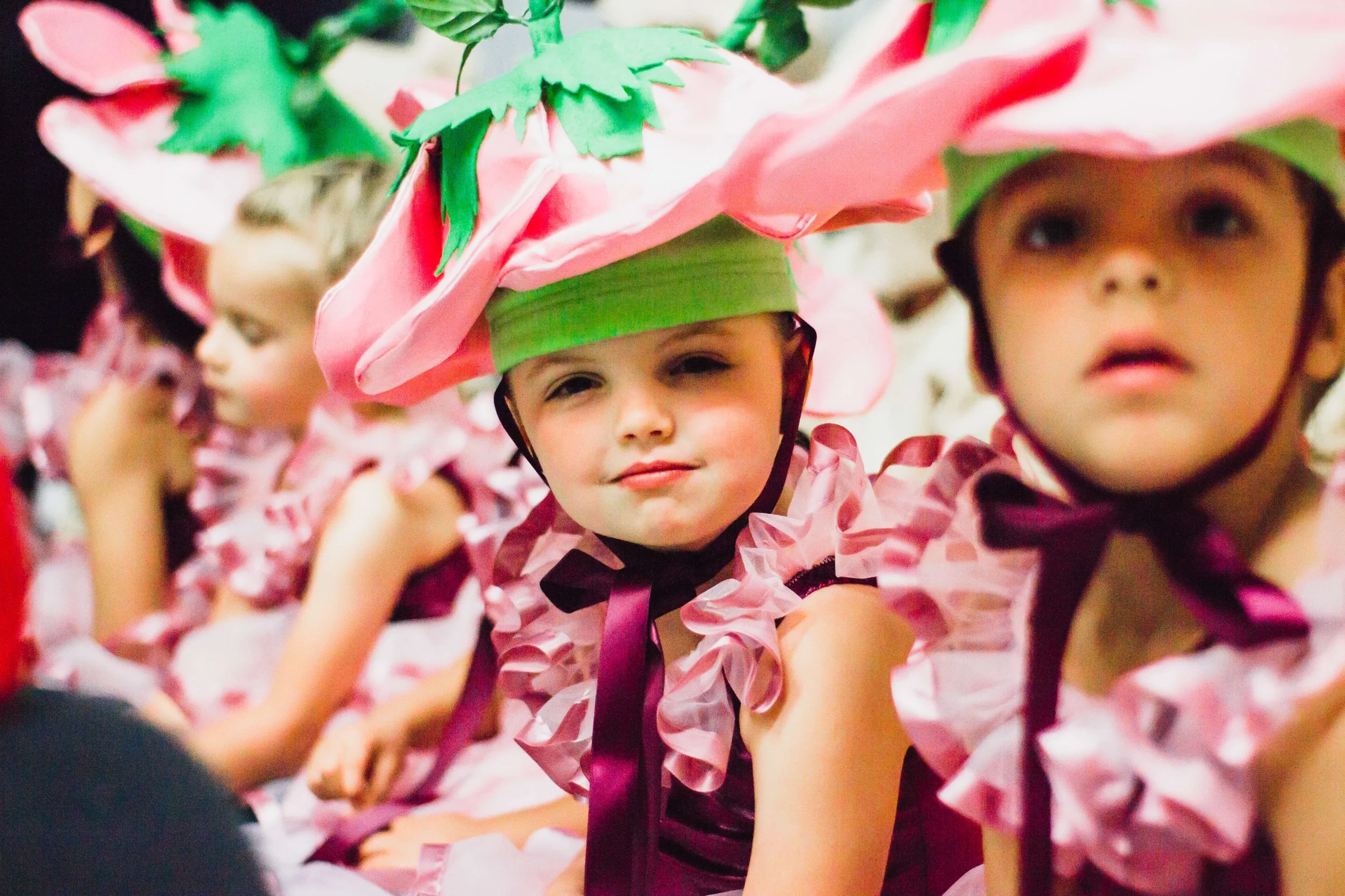 Children dressed in costumes resembling strawberries, with pink and green colors, participating in a performance or event.