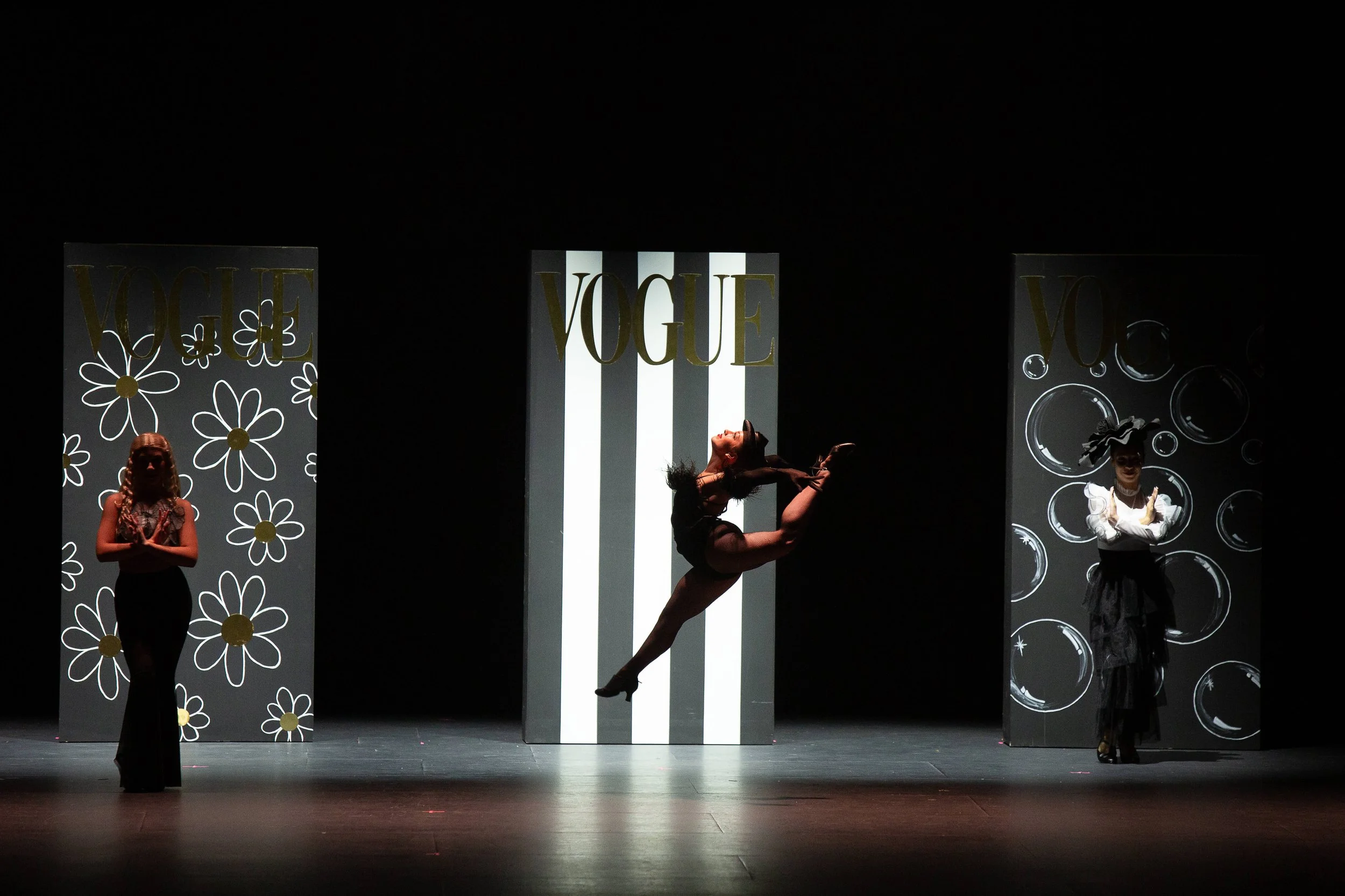 Stage with three performers and three large decorative panels with 'VOGUE' logos.