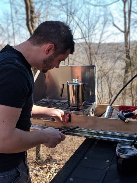 man lighting stove in truck bed kitchen drawer to make camp coffee