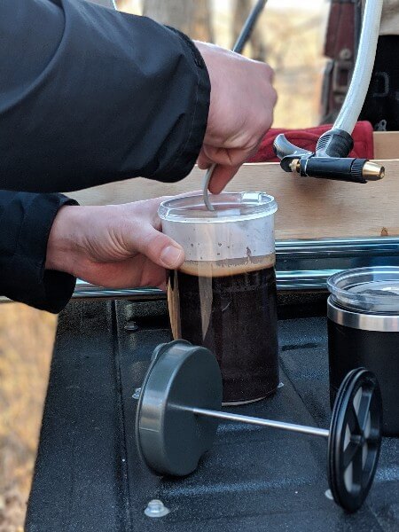 making french press camping coffee on tailgate of truck camper