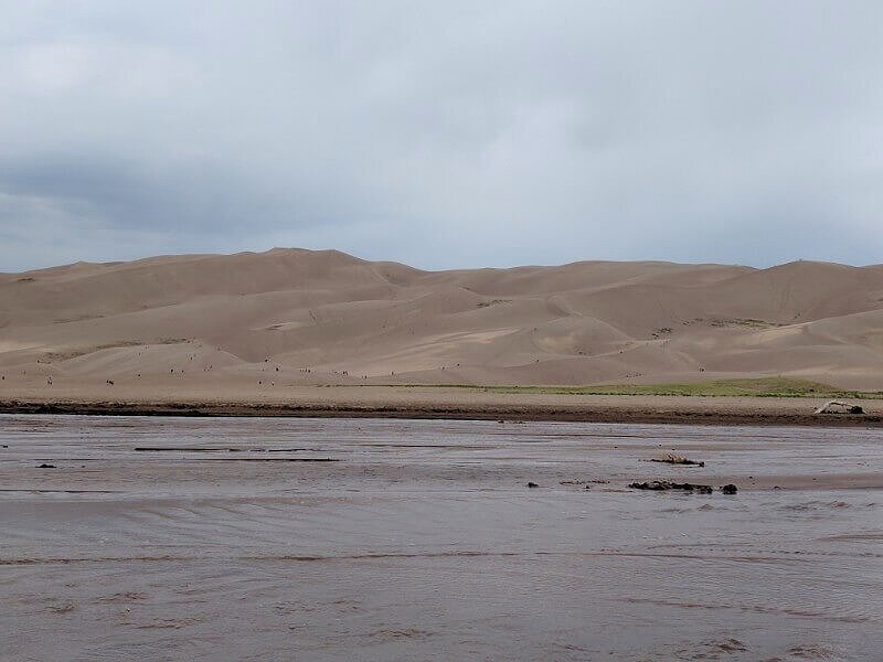 medano creek in front of sand dunes at national park colorado and people look tiny on dunes