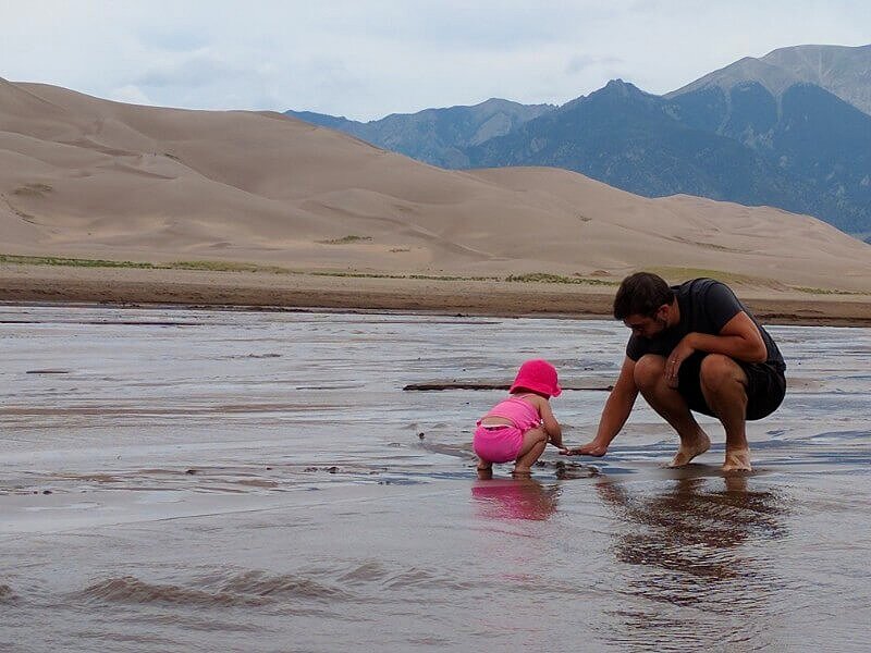 toddler and man playing in water and sand in medano creek colorado
