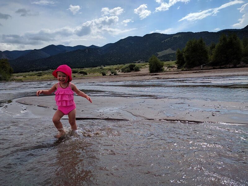 toddler wearing pink swimsuit running through shallow creek