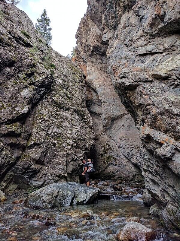 man with toddler in hiking backpack standing outside chasm at zapata falls colorado