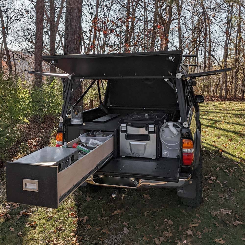 Toyota Tacoma truck camping sleeping platform drawer open with 12v fridge and water tank in bed