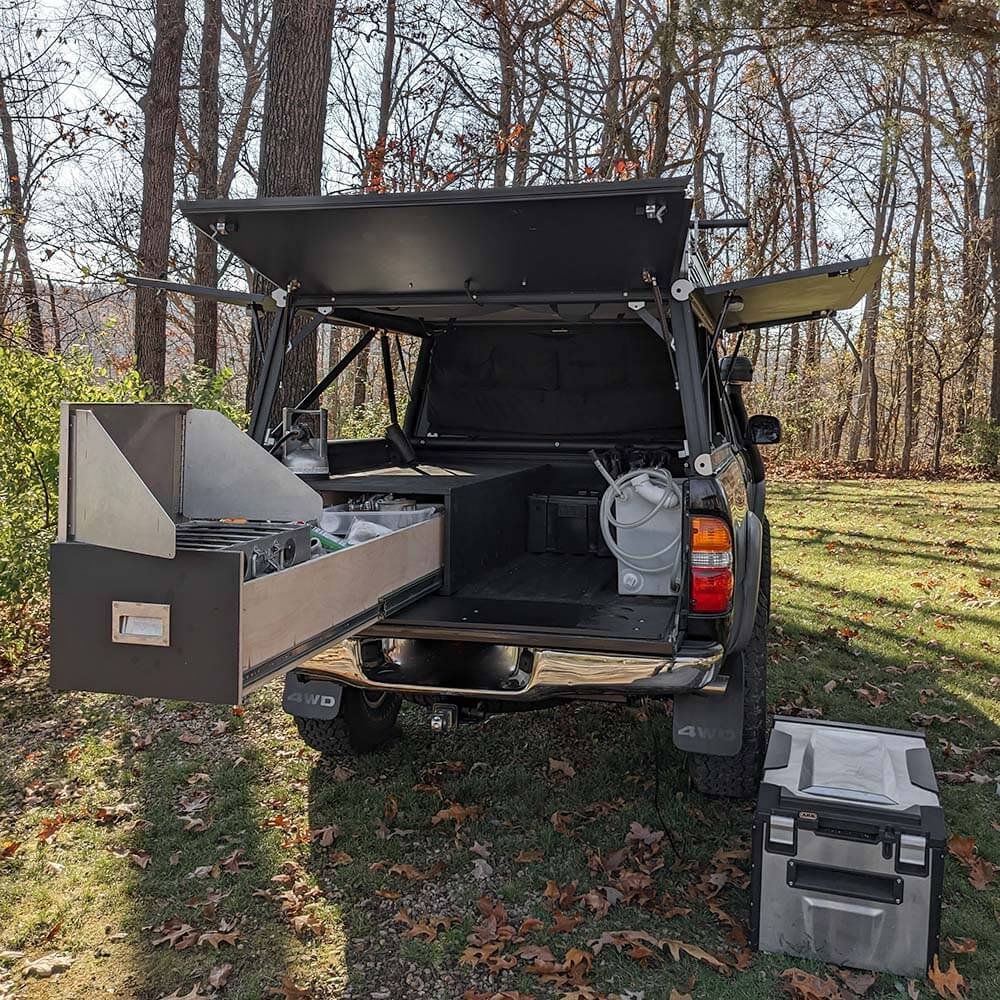 tacoma overland build truck bed drawer storage setup for camping with stove, 12v fridge, and 10 gallon water container