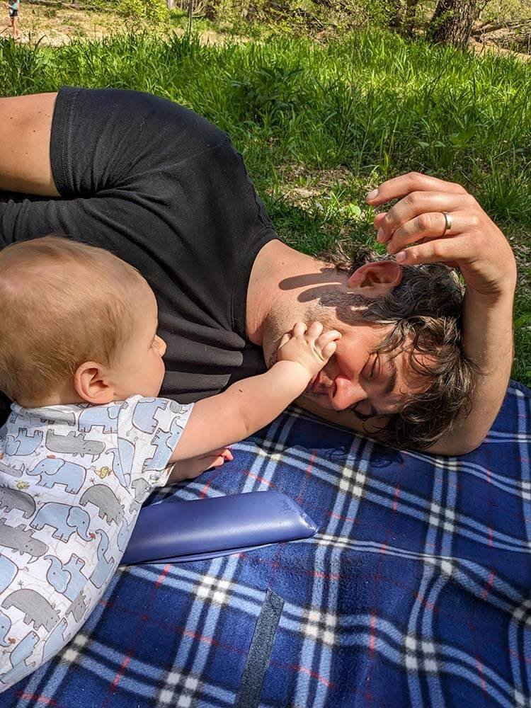 baby playing with dad on outdoor blanket while camping