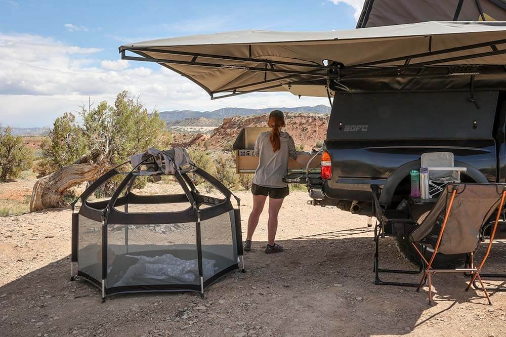 making food at camp while baby plays in portable play pen for camping